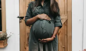 Kobieta w zielonej sukience obejmuje ciążowy brzuch. Pomimo obaw związanych z tokofobią, czeka na narodziny dziecka.