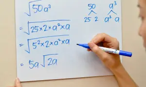 Eine Hand schreibt auf einem Whiteboard, wie man die Wurzel umschreibt: $\sqrt{50a^3}$ wird zu $5a\sqrt{2a}$ vereinfacht.