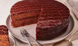 Eine glänzende Sacher Torte mit Schokoladenglasur und einem Stück Marmeladenfüllung. Gabeln liegen bereit.