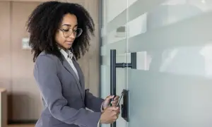 Donna con capelli ricci e occhiali apre una porta con uno smartphone, un modo moderno per vedere i dipendenti di un'azienda.