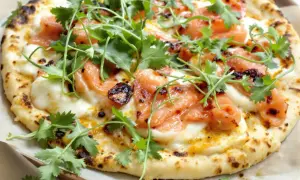Pizza saumon avec fromage fondant, garnie de coriandre fraîche et d'une touche de piment. Un délice visuel et gustatif.