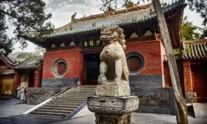 Kamienny lew strzeże wejścia do klasztoru Shaolin. Dwie postacie w szatach mnichów zbliżają się do schodów.