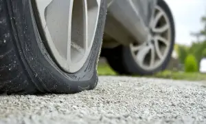 Uszkodzona opona w samochodzie, która powinna być typu runflat, leży płasko na żwirze.