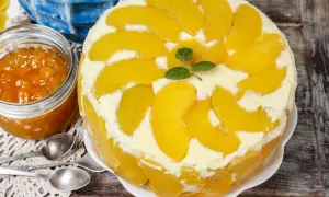 Eine köstliche Pfirsich Maracuja Torte, dekoriert mit frischen Pfirsichspalten und Minze. Daneben ein Glas Pfirsichmarmelade.