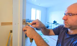 Un homme ajuste un bloc-porte sur un mur existant. Il utilise un outil pour s'assurer de la bonne pose.