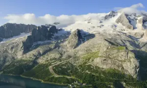 Majestätischer Marmolada Gletscher, umgeben von felsigen Gipfeln und grünen Hängen, mit einem See im Vordergrund.