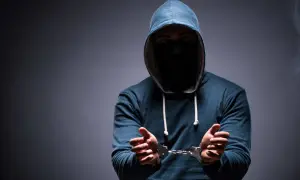 Mężczyzna w kapturze i masce na twarzy, z rękami w kajdankach, symbolizuje nadzieję na zatarcie skazania i nowy początek.