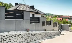 Nowoczesne ogrodzenie z betonu architektonicznego, z czarnymi elementami i kamiennym murkiem. Inspiracja, jak zrobić ogrodzenie z betonu architektonicznego.