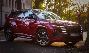 Czerwony Hyundai Tucson 2023 z czarnymi felgami i przyciemnianymi szybami, zaparkowany na tle kamienicy i drzew w jesiennym słońcu.