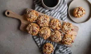 En bricka med åtta nyttiga frukostmuffins toppade med havre och mandel. En kopp kaffe och en muffin på en tallrik syns också.