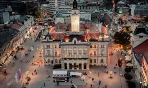 Abendliche Ansicht des Hauptplatzes in Novi Sad, Serbien, mit beleuchteten Gebäuden und Menschen, die spazieren gehen.
