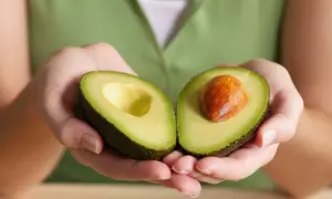 Manos sostienen un aguacate cortado por la mitad, mostrando su pulpa verde y el hueso. Así es qué es el aguacate, una fruta cremosa y nutritiva.