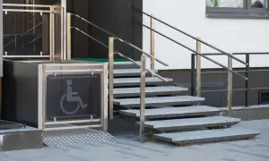 Un montascale con simbolo disabili, accanto a una scala esterna in metallo. La manutenzione è fondamentale per garantire l'accessibilità.