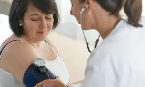 Lekarka bada ciśnienie pacjentce. Kobieta ma na ramieniu mankiet ciśnieniomierza, a lekarz słucha stetoskopem.