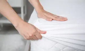Hands smoothing a white fitted sheet over a mattress. Is it ok to change bed sheets once a month? Probably not for optimal hygiene.