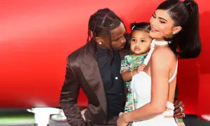 Kylie Jenner z dzieckiem i Travisem Scottem na tle czerwonej ściany.