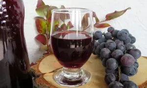 Ciemnoczerwone wino w kieliszku, obok kiść winogron i butla. Idealne do domowego wina w 5 litrowej butli.