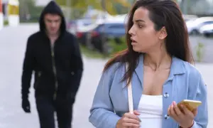 Przerażona kobieta z telefonem w ręku czuje, że jest śledzona. Mężczyzna w kapturze idzie za nią.