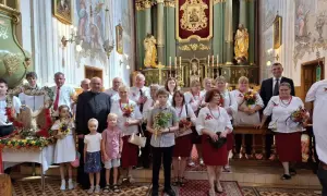 Uroczystość Wniebowzięcia Najświętszej Maryi Panny w kościele. Grupa osób w strojach ludowych i duchowny pozują do zdjęcia.