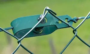 Grüner Drahtspanner hält den Maschendrahtzaun straff.