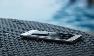 Smartfon z kroplami wody na ekranie, leżący na plecionej powierzchni. To dowód, że IP68 co oznacza – pełną ochronę przed pyłem i zanurzeniem w wodzie.