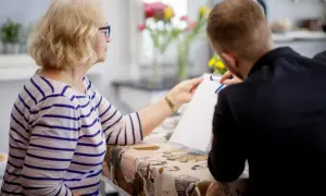 Starsza kobieta i młody mężczyzna przy stole z dokumentami.