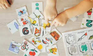 Manos de niños jugando con tarjetas de aprendizaje, practicando ejercicios de memoria con imágenes de animales, números y objetos.