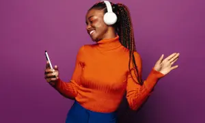 A woman with braids and headphones smiles, holding a phone. She's a visual representation of how to get your music on playlists.