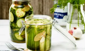 Två glasburkar fyllda med krispig, picklad gurka, dill och kryddor. En gaffel ligger bredvid.
