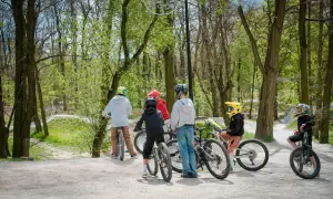 Grupa dzieci w kaskach odpoczywa na rowerach na bielszowice trails. W tle widać leśną ścieżkę rowerową.