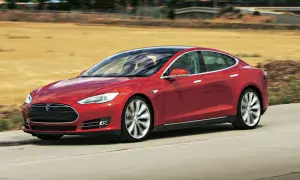 Czerwony Tesla Model S pędzi po drodze, otoczony suchymi, trawiastymi krajobrazami.