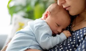 Mutter hält ihr schlafendes Baby. Der leichte baby haarausfall ist kaum sichtbar, während das Kind friedlich an ihrer Brust ruht.