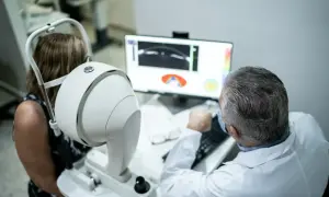Lekarz bada pacjentkę za pomocą urządzenia do angiografii oka. Dowiedz się, jak się przygotować do badania.