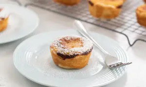 Un delizioso pastel de nata, cosparso di zucchero a velo, su un piatto azzurro con una forchetta.
