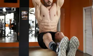 Uomo con addominali bassi scolpiti, appeso a una sbarra in palestra, con focus sui muscoli addominali.