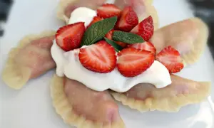 Pyszne pierogi z truskawkami, polane śmietaną i ozdobione świeżymi owocami i miętą. Letnia uczta na talerzu.