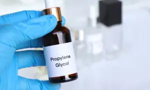 Ręka w niebieskiej rękawiczce trzyma buteleczkę z etykietą "Propylene Glycol".