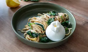 Zitronen Pasta mit Spinat und Burrata auf einem grünen Teller, daneben eine Zitronenhälfte.