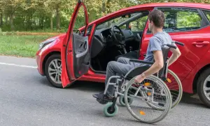 Uomo in carrozzina accanto a un'auto rossa, pronto per il passaggio di proprietà auto disabile decesso.