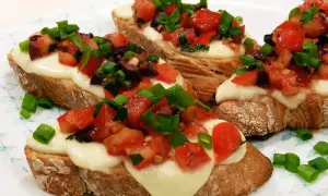 Bruschetta z pomidorami i mozzarellą: chrupiące grzanki z roztopionym serem, świeżymi pomidorami, oliwkami i szczypiorkiem. Idealny przepis na szybką przekąskę.