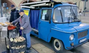 Sprzedawca przygotowuje kiełbaski z niebieskiej Nyski. Obok stoją bułki i drewno na opał.