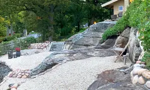 En vacker stenlagd uteplats med grusgångar, stenmurar och trappor som leder upp mot ett hus. En inspiration för en naturlig och robust utomhusmiljö.