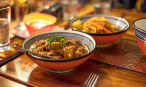 En skål med mustig gryta, en klassiker inom sydafrikansk mat, serveras med en gaffel. I bakgrunden syns en annan skål med grönsaker och en flammande ljuslykta.