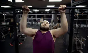 Uomo con fisico endomorfo si allena in palestra, concentrato su una trazione alla sbarra.