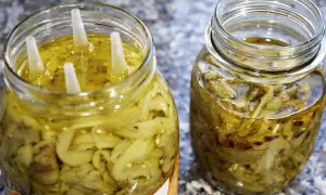 Due barattoli di melanzane a filetti sott'olio, uno con quattro tappi bianchi che emergono dall'olio dorato.