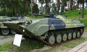 Czołg BMP, czyli bojowy wóz piechoty, z charakterystycznym kamuflażem. W tle las i inne pojazdy wojskowe.