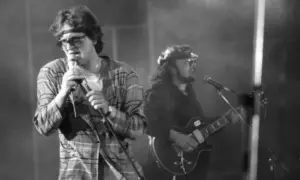Wokalista z opaską na głowie i w kratę śpiewa do mikrofonu, obok gitarzysta. Widać, że perfect wszystko ma swój czas, nawet na scenie.