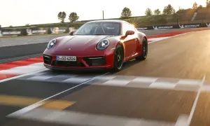 Czerwone Porsche 911 GTS sunie po torze wyścigowym, odbijając promienie zachodzącego słońca.