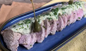Tranches de vitello tonnato, nappées d'une sauce crémeuse et garnies de câpres et de persil, sur un plat bleu.