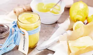 En burk med krämig lemon curd, redo för ett recept. Citroner och smör ligger bredvid.